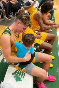 Assistant Coach Ashley Webster's infant son, Aiden, being held by a Saint Leo Men's basketball player.