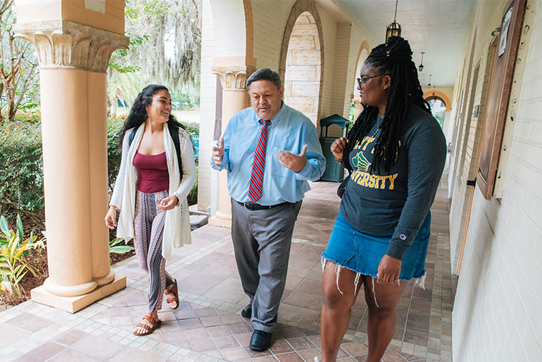 Ed Dadez, Saint Leo University President, walking down the hallway talking to students.